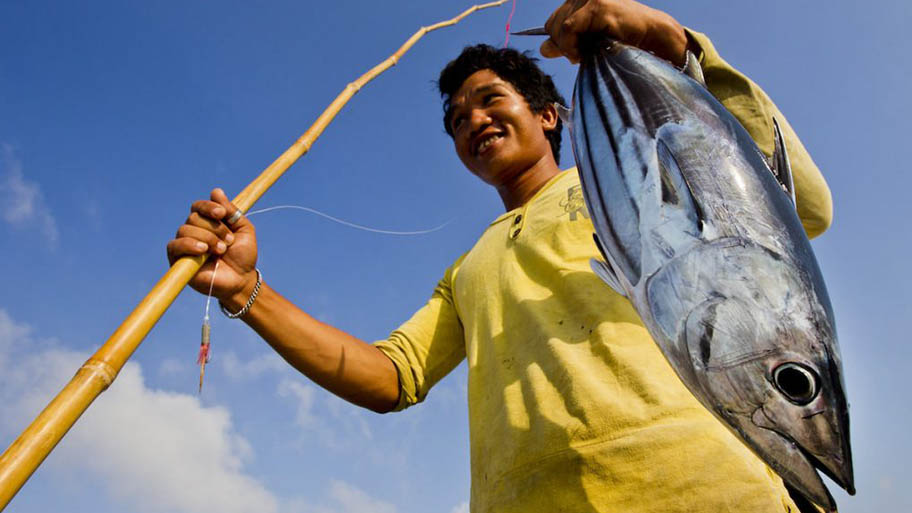 Man with pole and line holding freshly caught tuna